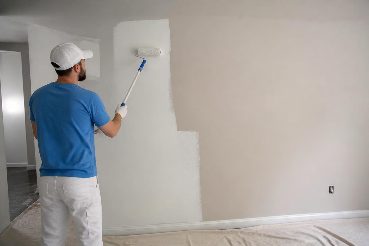 Maler streicht mit der Farbrolle eine Wand in einem leeren Raum