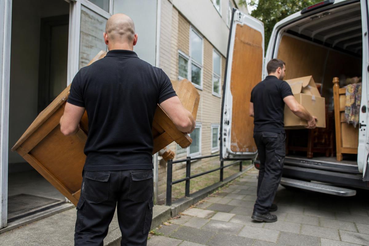 Mitarbeiter tragen Kartons und Möbel aus einer Wohnung zum Transporter